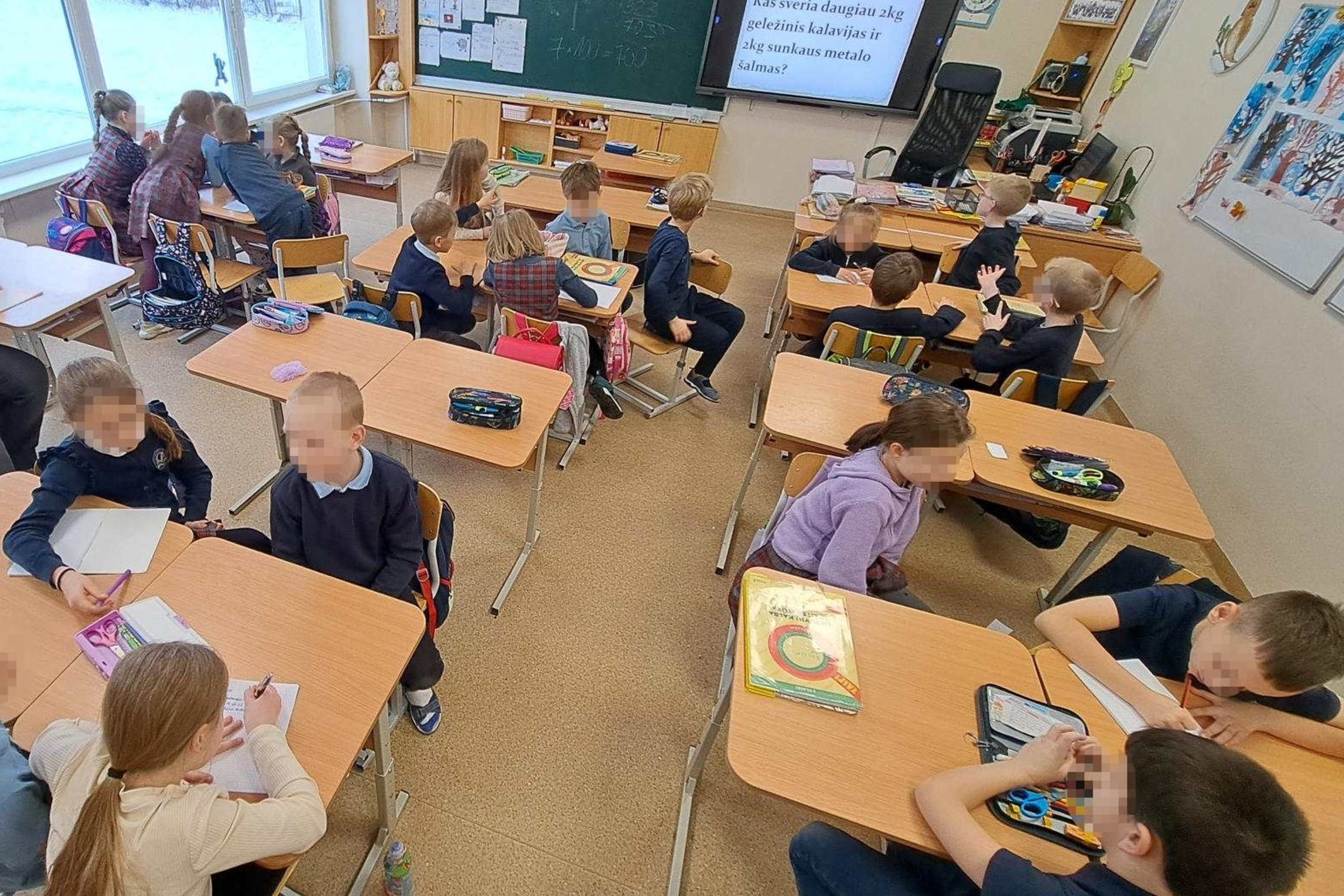 Mokyklos klasėje mokiniai sėdi suoluose ir dalyvauja edukacijoje, ekrane matomas klausimas, vaikai rašo ir diskutuoja protmūšio metu.