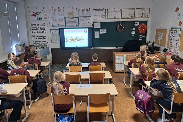 Klasėje prie suolų sėdi Vilniaus Filaretų pradinės mokyklos mokiniai, stebintys ekrane rodomą pristatymą apie Lietuvos didžiuosius kunigaikščius ir Vilniaus pilis.