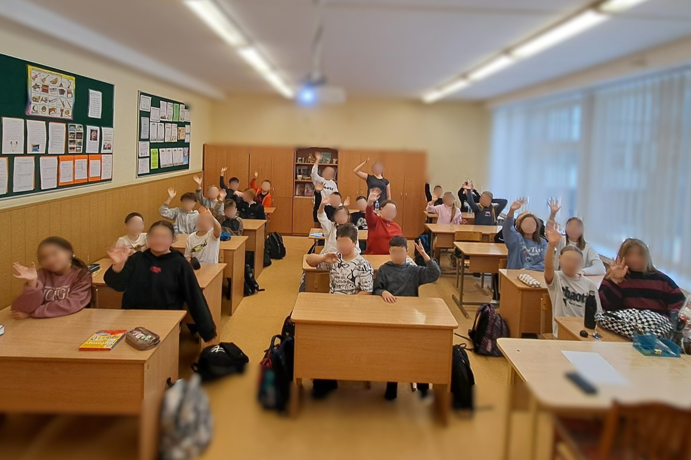 Nuotraukoje klasė pilna vaikų. Vaikai sėdi suoluose ir mojuoja. Atrodo patenkinti ir linksmi, galimai jiems patiko edukacija.