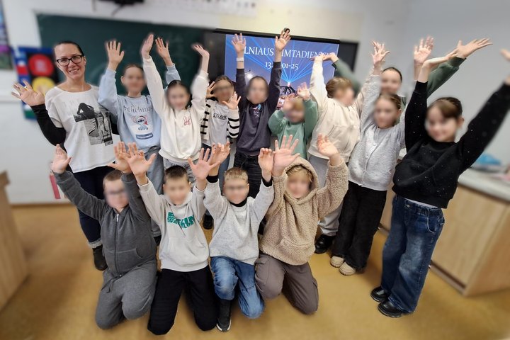 Nuotraukoje vaikai ir edukatorė. Visi mojuoja pakėlę rankas. Po edukacijos nuotaikos puikios.