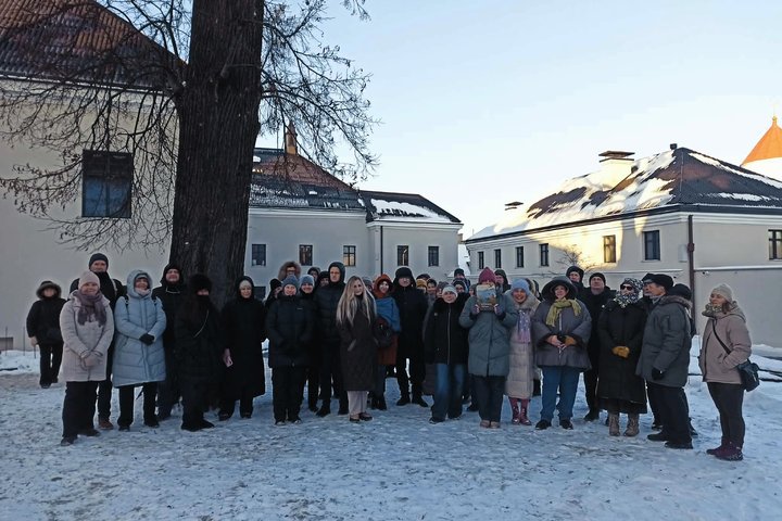 Ekskursijos dalyviai stovi Vilniaus pilių teritorijoje žiemą, tarp istorinių pastatų, apsirengę šiltais drabužiais.