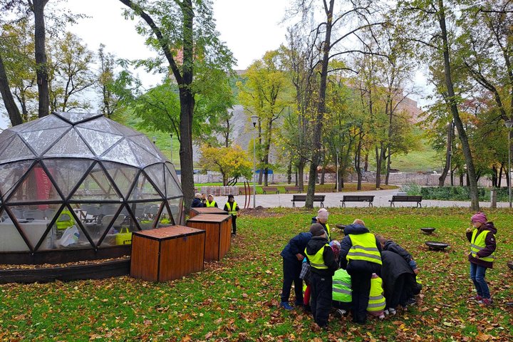 Vilniaus Gabijos progimnazijos antrokai edukacinės pamokos „Nuo išlikimo iki žinios: ugnies kelias per amžius“ metu susibūrę atlieka praktinę užduotį lauke. Šalia Vilniaus pilių kupolo, rudenėjančių medžių apsuptyje, mokiniai tyrinėja ugnies istoriją.