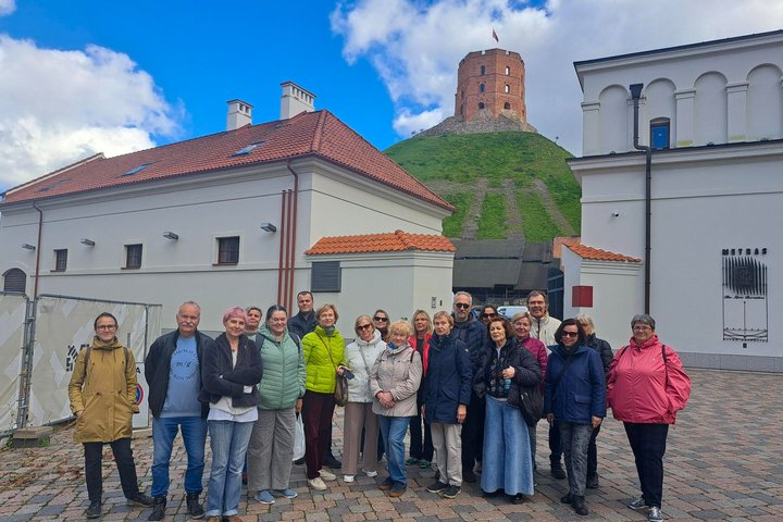 Ekskursijos „Valdovas spaudžia leteną: Vilniaus pilių šunys“ dalyviai pozuoja bendroje nuotraukoje Vilniaus pilių teritorijoje. Fone matyti Gedimino kalnas ir Aukštutinės pilies bokštas.