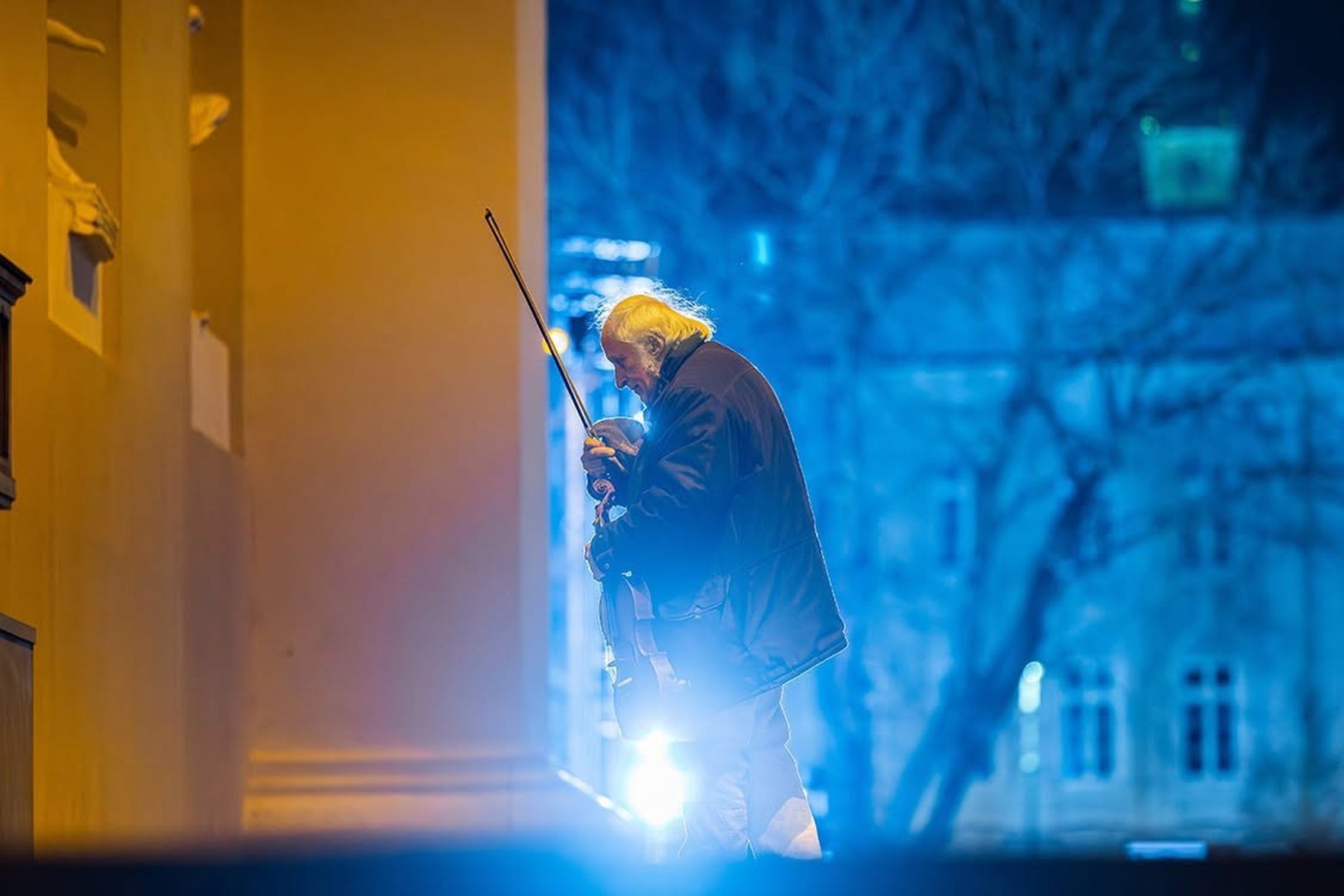 Altininkas Andrius Pleškūnas su instrumentu Vilniaus katedros prieangyje, mėlynų ir šiltų šviesų fone.