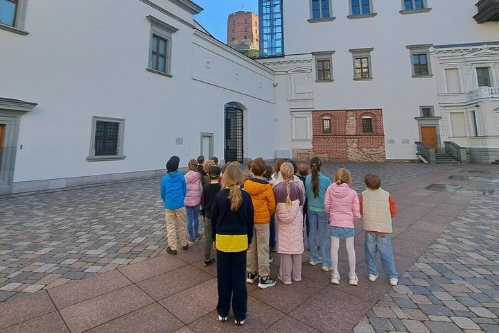 Nuotraukoje vaikai, Valdovų rūmų kieme, žiūri į Aukštutinės pilies bokštą.  Jie dalyvauja edukacinėje pamokoje  „Gediminas ir Vilniaus trys pilys“