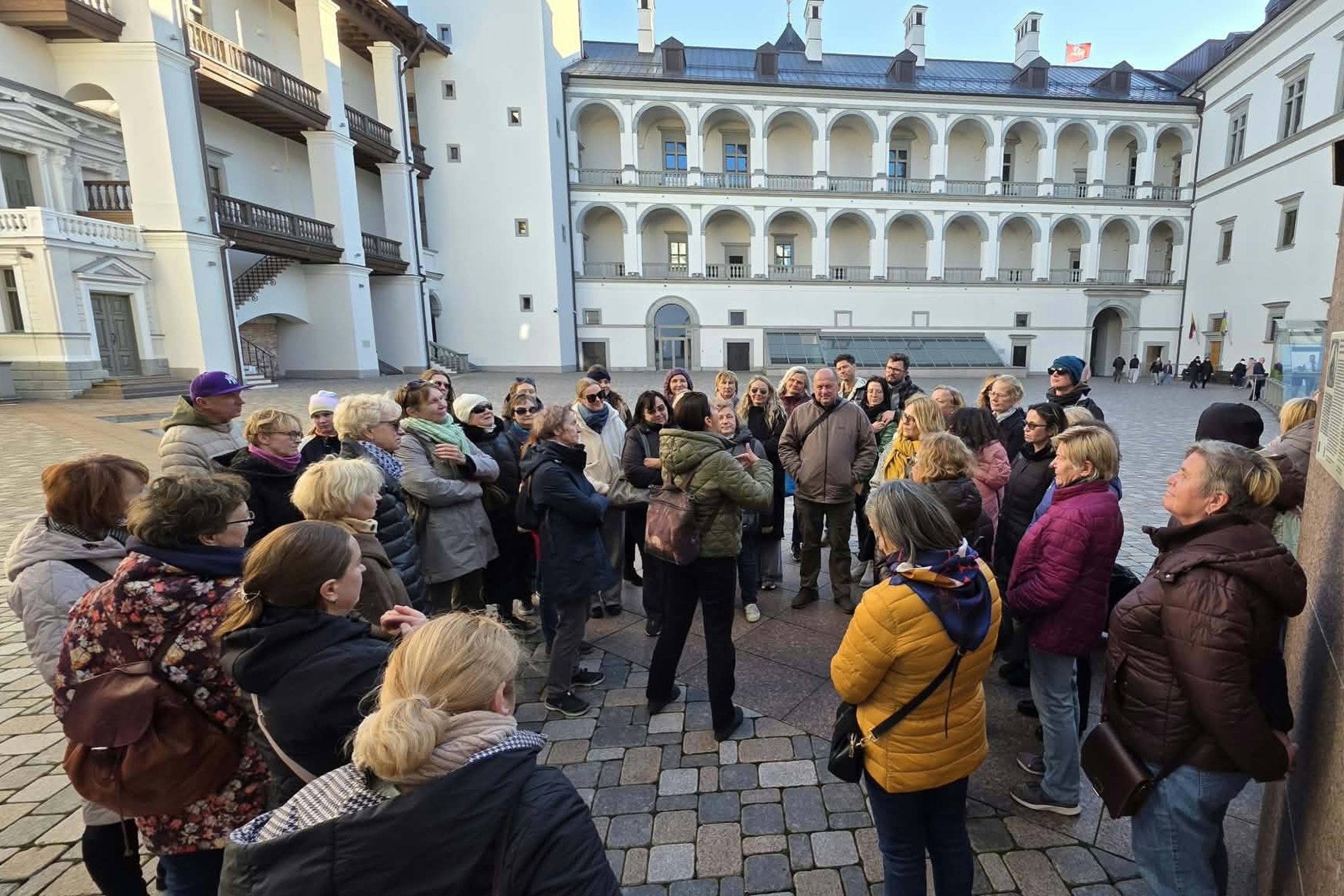 Ekskursijos dalyviai Vilniaus pilių teritorijoje, Valdovų rūmų kieme, klausosi pasakojimo apie XVI–XVII a. valdovų dvaro meistrus, jų darbus ir privilegijas.