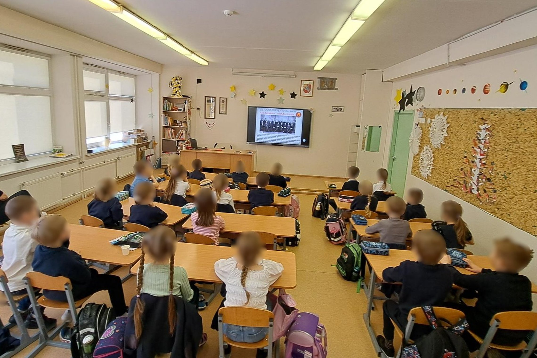 Nuotraukoje vaikai klasėje, sėdi suoluose, dalyvauja edukacijoje „Vasario 16-oji ir Vilniaus pilys“, ekrane matome nuotrauką su Nepriklausomybės Akto signatarais.
