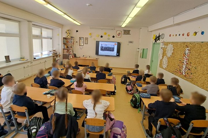 Nuotraukoje vaikai klasėje, sėdi suoluose, dalyvauja edukacijoje „Vasario 16-oji ir Vilniaus pilys“, ekrane matome nuotrauką su Nepriklausomybės Akto signatarais.