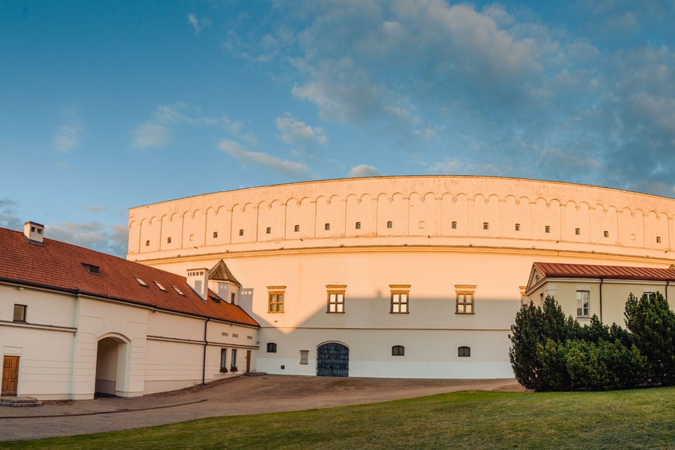 Vilniaus pilių teritorijoje esantis Senasis arsenalas – šviesių sienų, apvalios formos istorinis pastatas su mažais langais, vakaro saulės apšviestas vidiniame kieme.
