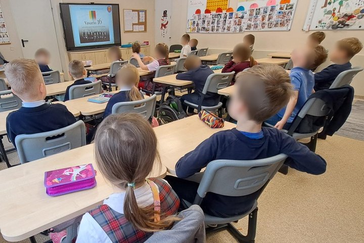 Nuotraukoje mokiniai. Jie sėdi suoluose ir žiūri į ekraną. Dideliame ekrane matome Lietuvos tarybos narius.