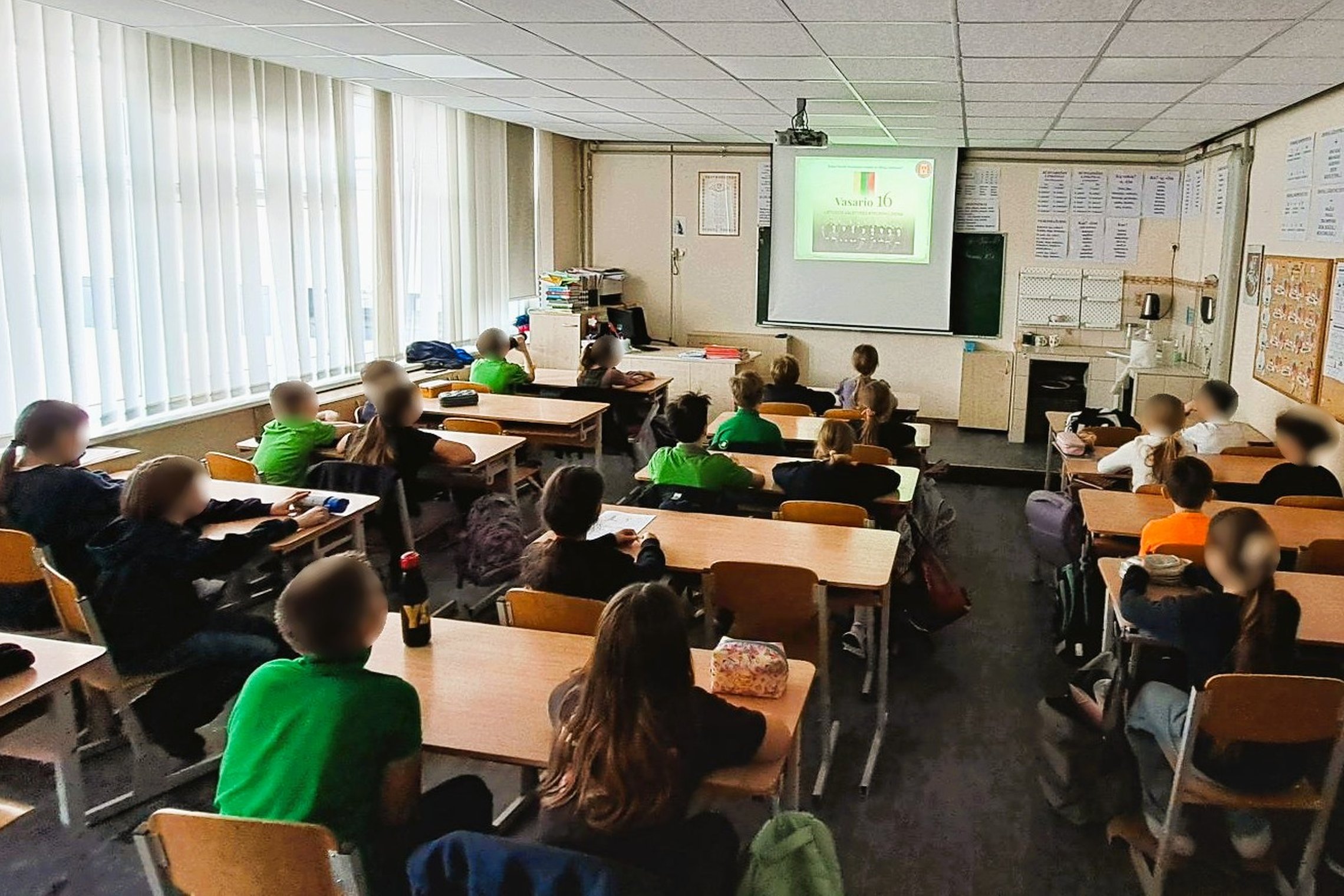 Nuotraukoje mokiniai klasėje. Sėdi suoluose ir žiūri į ekraną. Ekrane Vasario 16-osios Akto signatarai