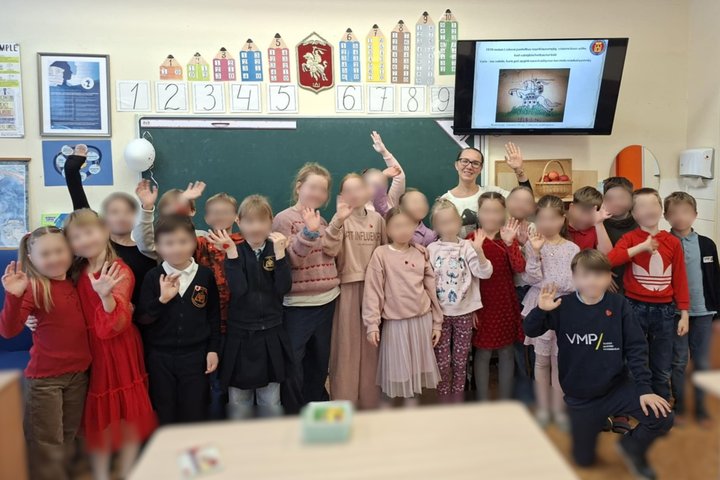 Nuotraukoje mokiniai ir edukatorė sustoję bendrai nuotraukai po edukacijos. Visi šypsosi ir mojuoja. 