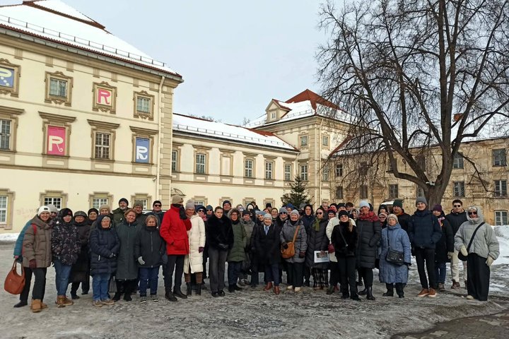 Gausi ekskursijos dalyvių grupė stovi priešais istorinius rūmus su Radvilų ženklu languose; saulėta žiemos diena, ant žemės matyti sniego likučiai.