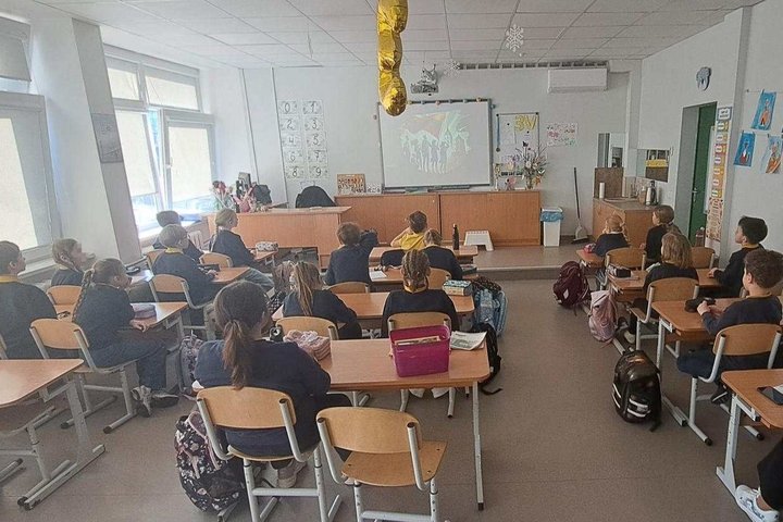 Trečiokai klasėje sėdi suoluose ir stebi pristatymą apie laisvę, rodomą projektoriaus ekrane edukacijos metu.