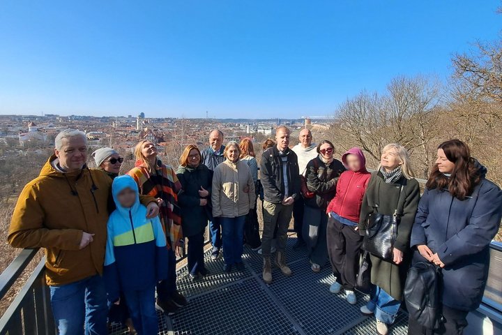 Nuotraukoje grupė žmonių stovi Altanos bokštelio terasoje. Už jų atsiveria viena gražiausių Vilniaus panoramų – senamiesčio bokštai, stogai ir miesto horizontas.