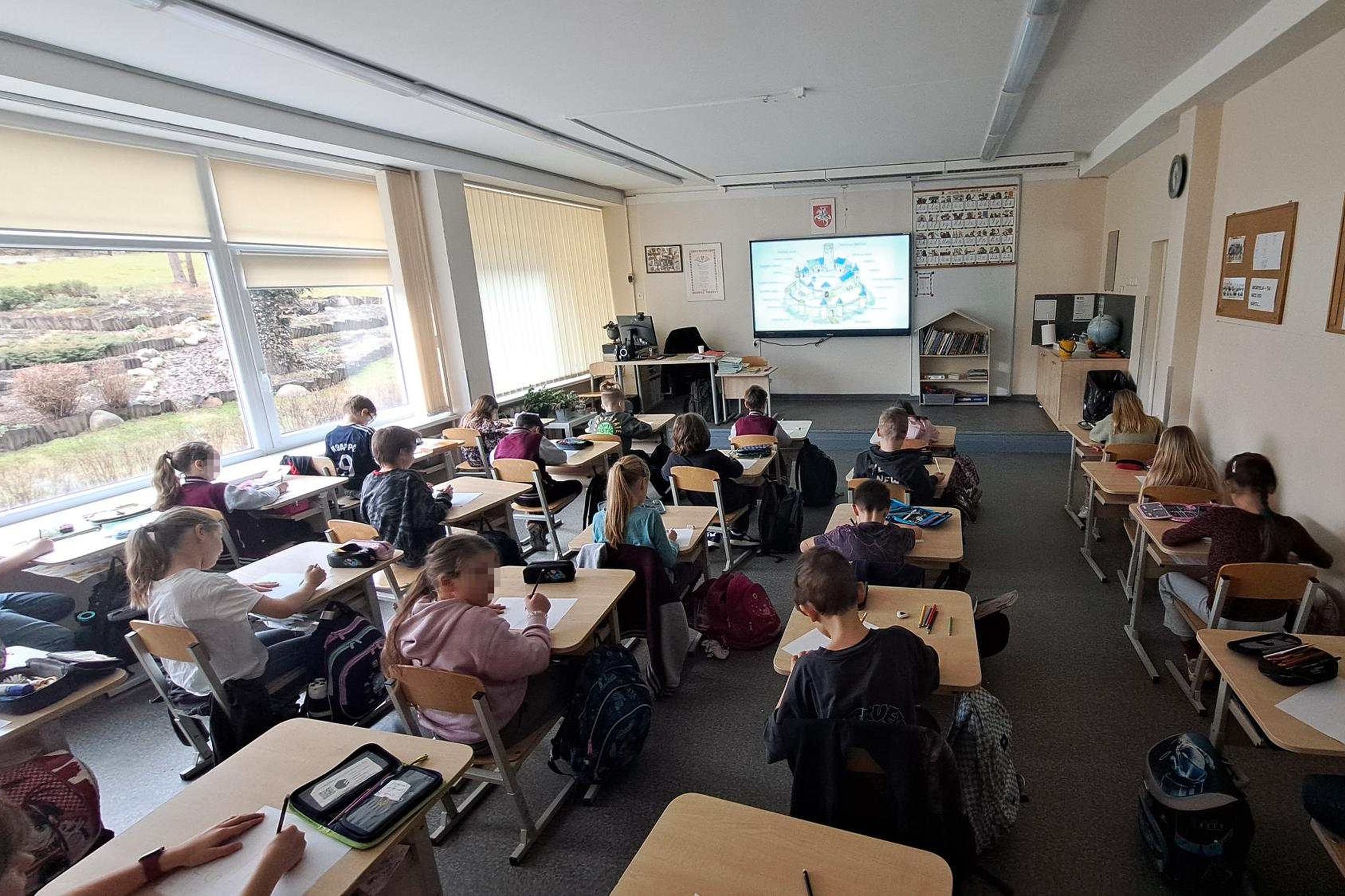 Antrokai klasėje sėdi prie suolų ir atlieka užduotį, o priekyje ekrane rodoma skaidrė apie Vilniaus pilis, vyksta edukacija apie viduramžių pilis.
