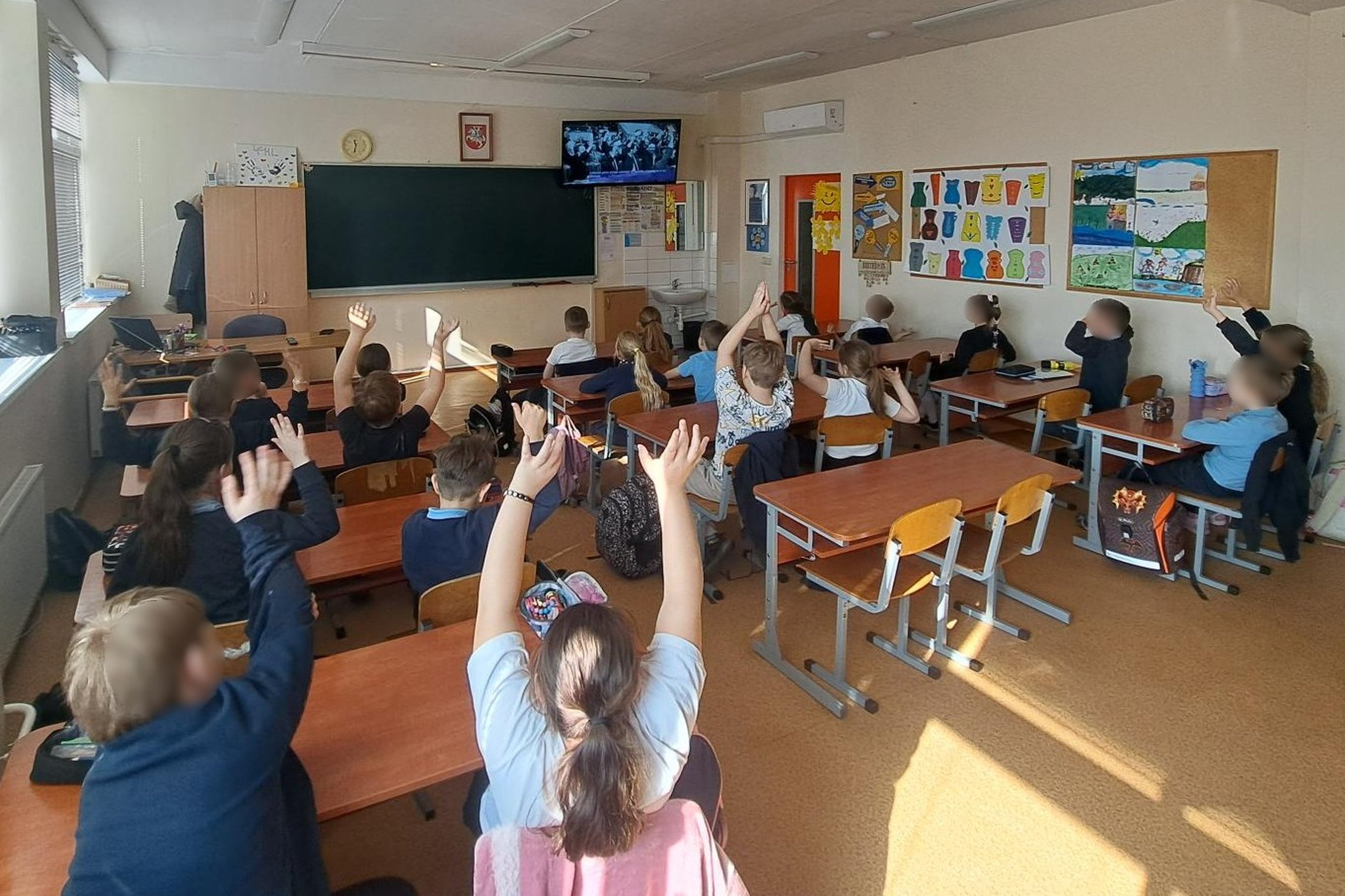 Nuotraukoje mokiniai klasėje. Jie sėdi suoluose. Ekrane Kovo 11-osios nuotrauka. Mokiniai dalyvauja edukacijoje šia tema.