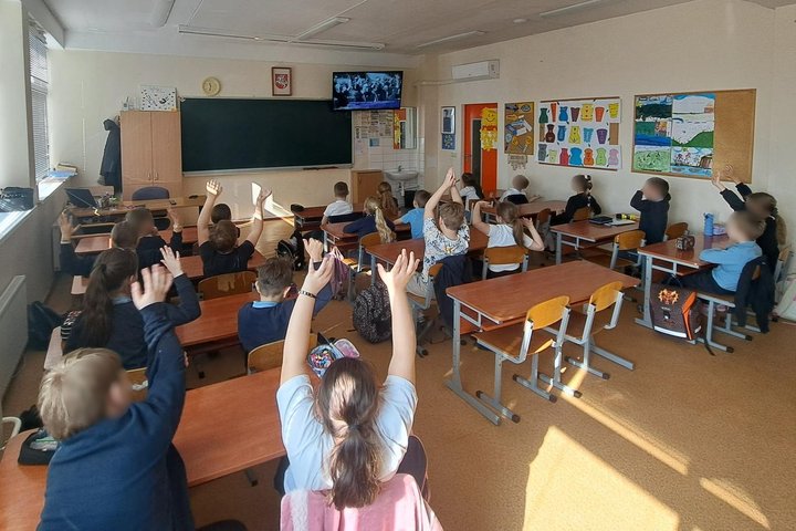 Nuotraukoje mokiniai klasėje. Jie sėdi suoluose. Ekrane Kovo 11-osios nuotrauka. Mokiniai dalyvauja edukacijoje šia tema.