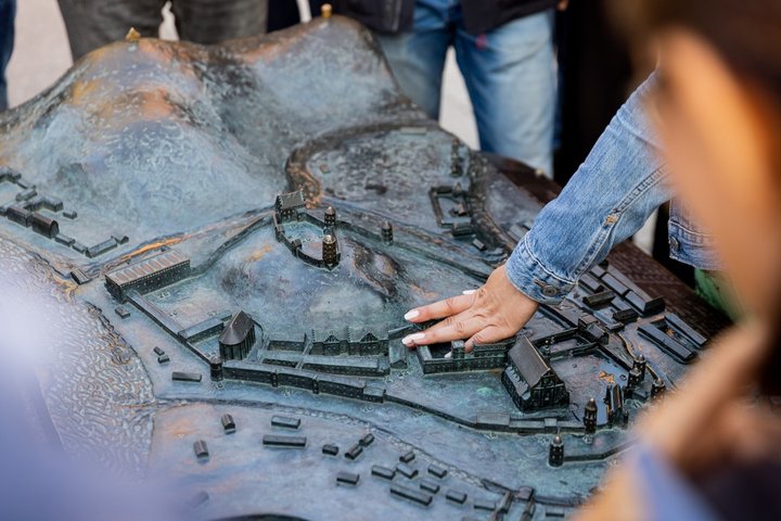 Žmogaus ranka liečia bronzinį Vilniaus pilių maketą su pastatais ir gynybinėmis sienomis.