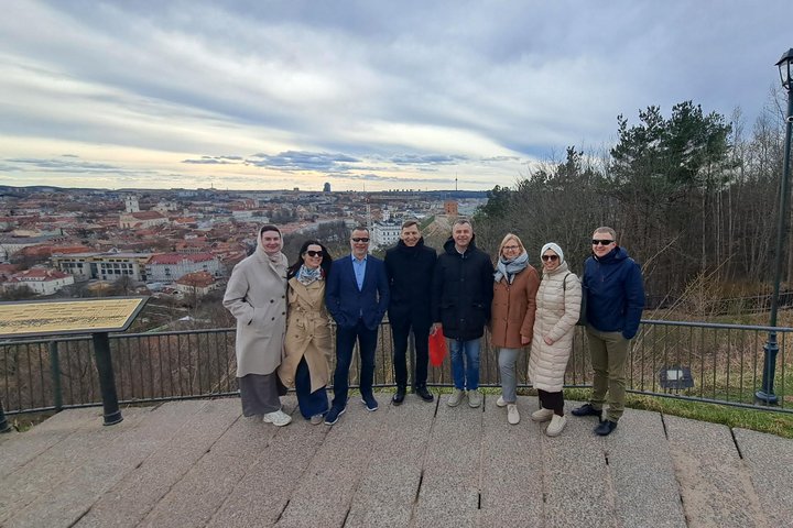 RIMI vadovų kolektyvas stovi Vilniaus pilių teritorijoje esančioje apžvalgos aikštelėje, fone atsiveria Vilniaus senamiesčio panorama.
