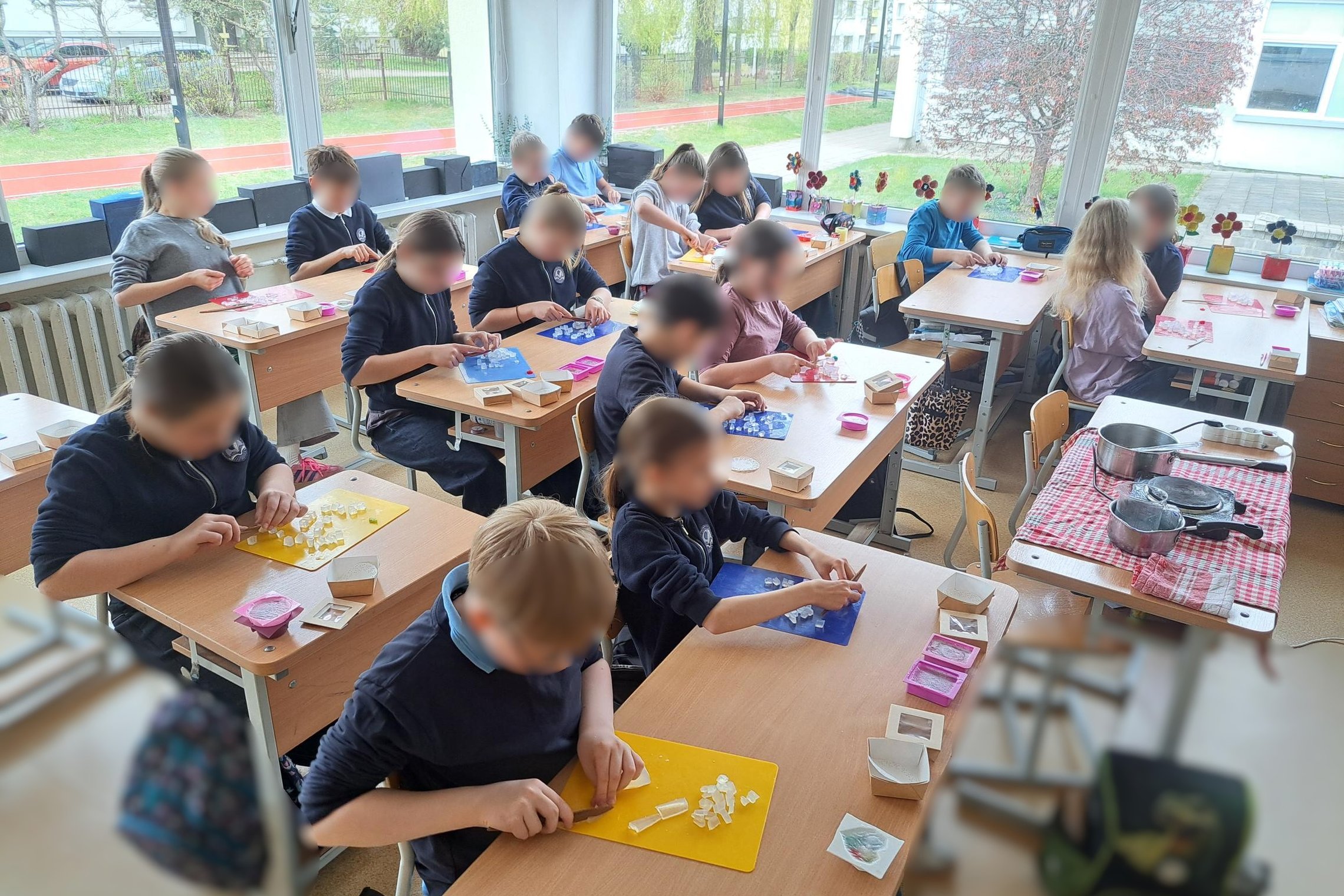 Mokiniai klasėje gamina muilą – prie stalų pjausto muilo pagrindą, dėlioja gabalėlius ir ruošia savo kūrinius edukacijos metu.