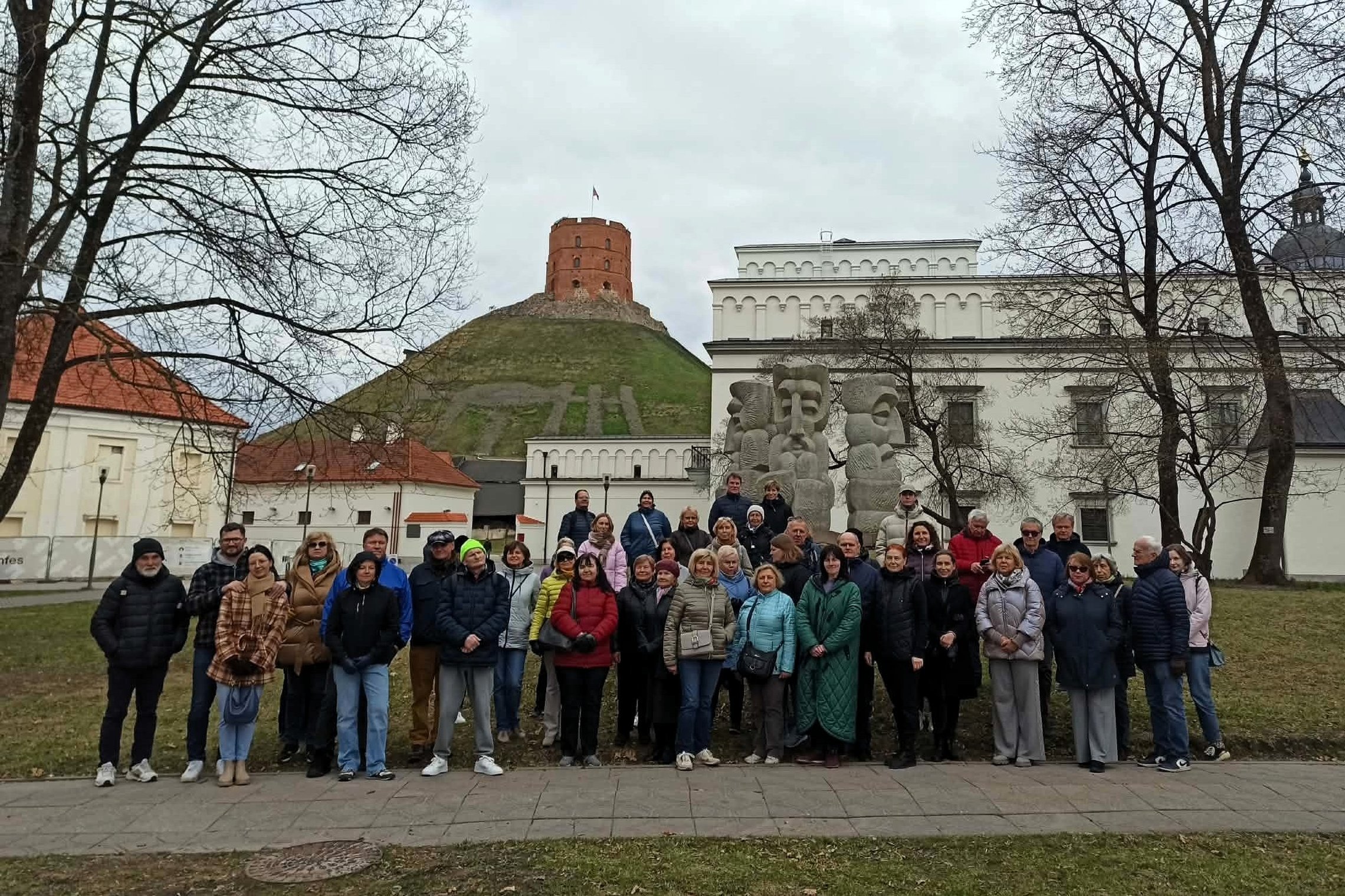 Didelė žmonių grupė stovi Vilniaus pilių teritorijoje prie skulptūros, fone matyti Gedimino pilies bokštas ant kalno ir Valdovų rūmai.