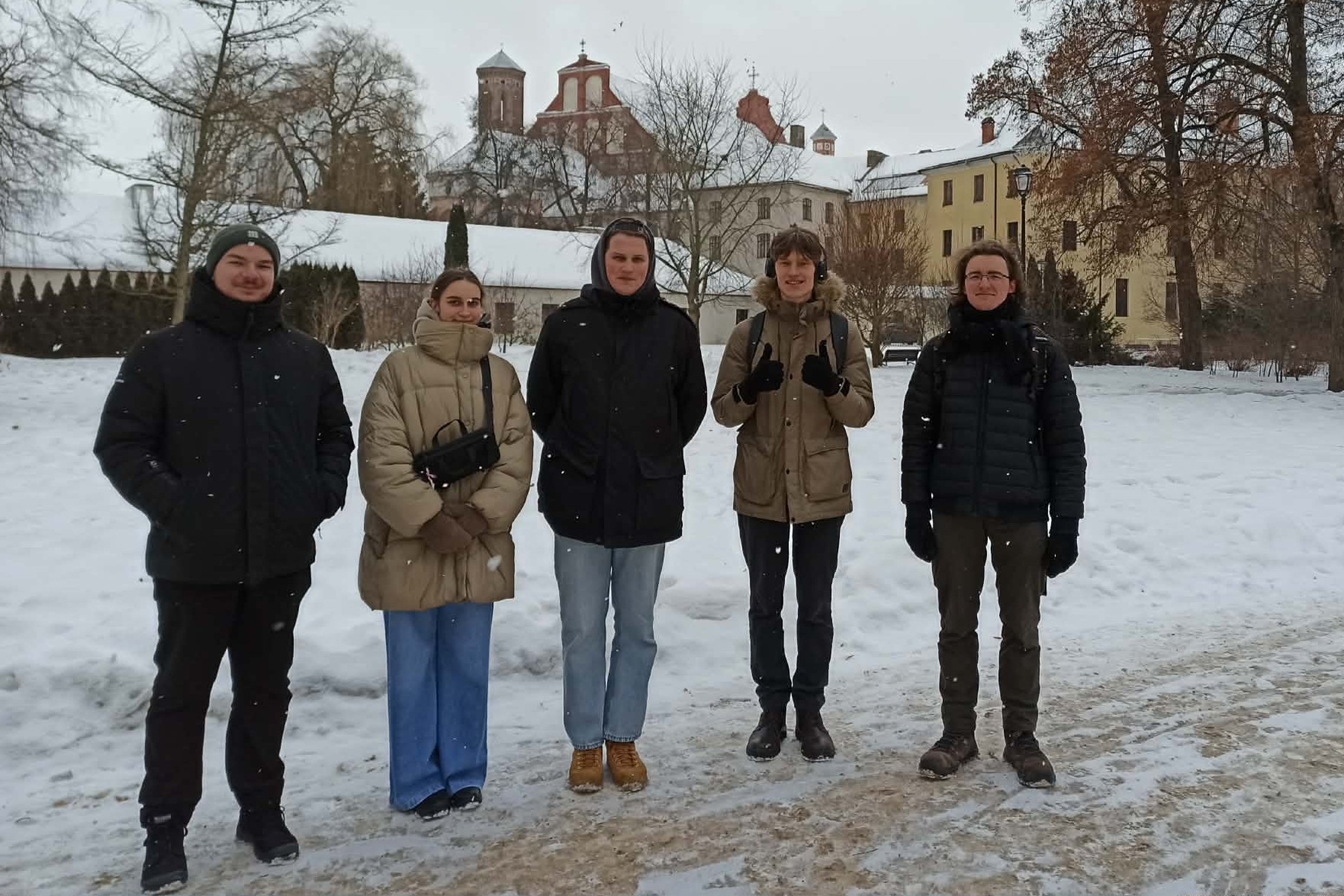 Penki Vilnius Tech studentai stovi snieguotoje Vilniaus pilių teritorijoje, fone matyti bažnyčios bokštai ir senamiesčio pastatai.