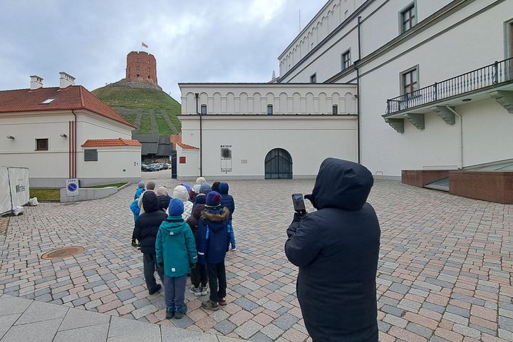 Vaikų grupė su pedagogu Vilniaus pilių kieme, tolumoje matoma Gedimino pilies bokštas ant kalno