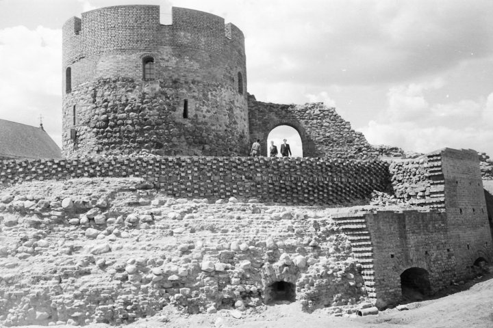 Juodai balta nuotrauka, kurioje matoma Kauno pilis 1960 m.: apvalus mūrinis bokštas ir iš dalies atstatytos pilies sienos. Prie arkos stovi keli žmonės, o priekyje matyti senesnių mūrų ir pamatų fragmentai.