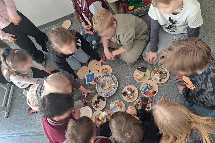 Nuotraukoje mokiniai susėdę ratu, tyrinėja radinius, kuriuos surinko edukacijos metu.