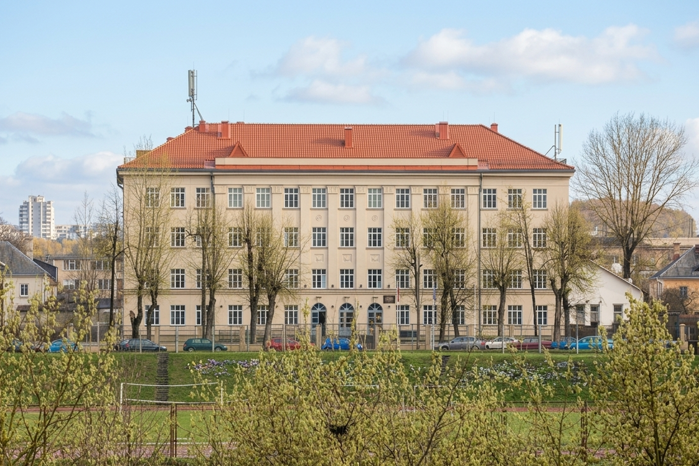 Vilniaus Šolomo Aleichemo gimnazijos pastatas – šviesi, trijų aukštų mokykla su raudonu stogu, matoma iš priekio, priešais ją – žalioji zona su medžiais ir sporto aikštynu.