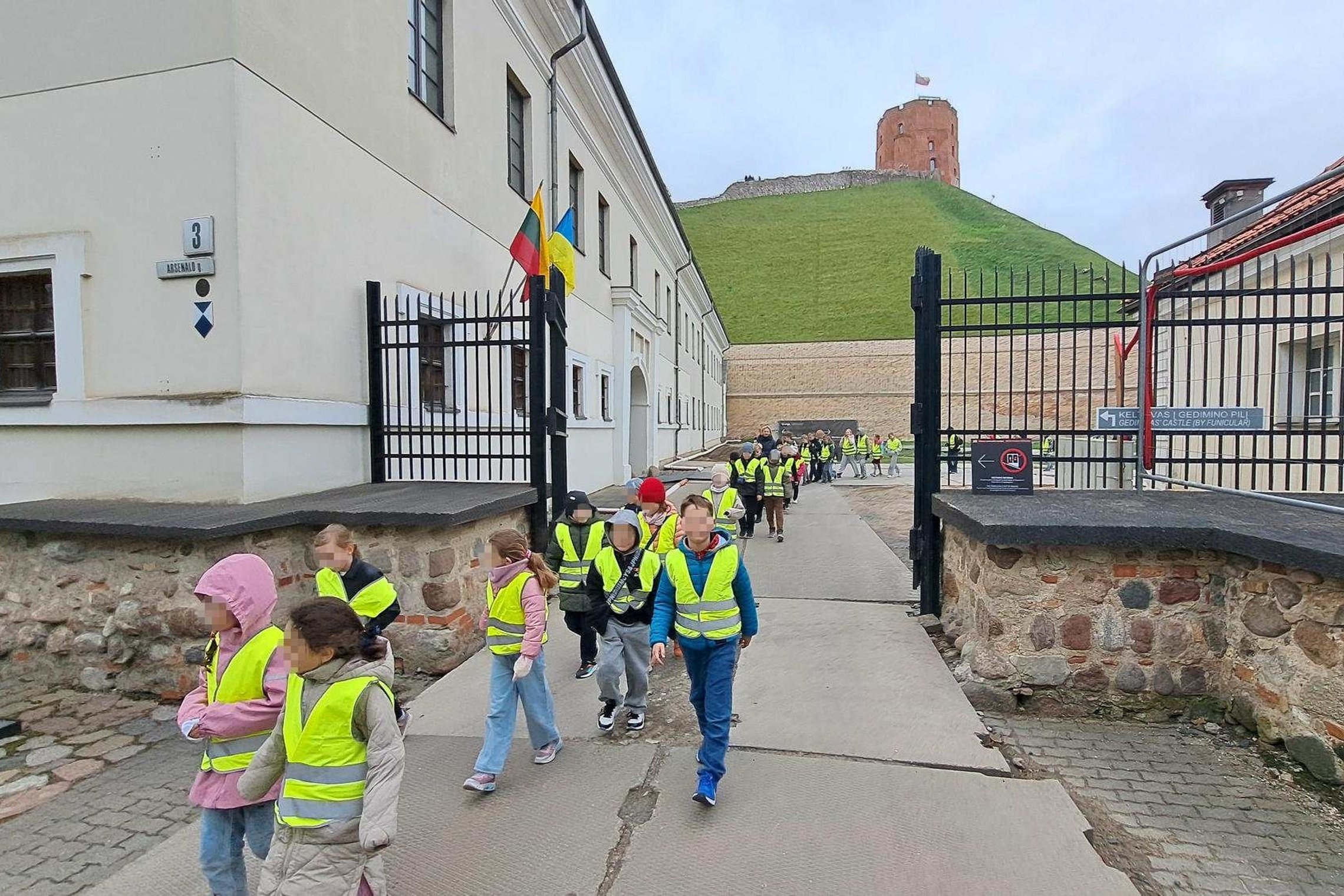Vaikai su ryškiomis saugos liemenėmis eina Vilniaus pilių teritorijoje link Gedimino pilies bokšto edukacinės ekskursijos metu.