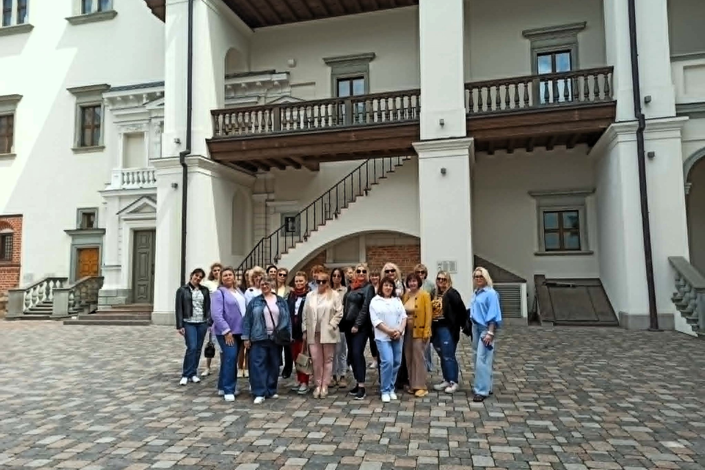 Grupė ekskursijos dalyvių pozuoja Vilniaus pilių teritorijoje, istorinio pastato kieme.
