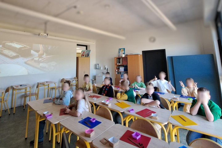 Nuotraukoje mokyklos klasė su suolais. Juose sėdi mokiniai. Jie dalyvauja edukacijoje „Muilo kodas“.