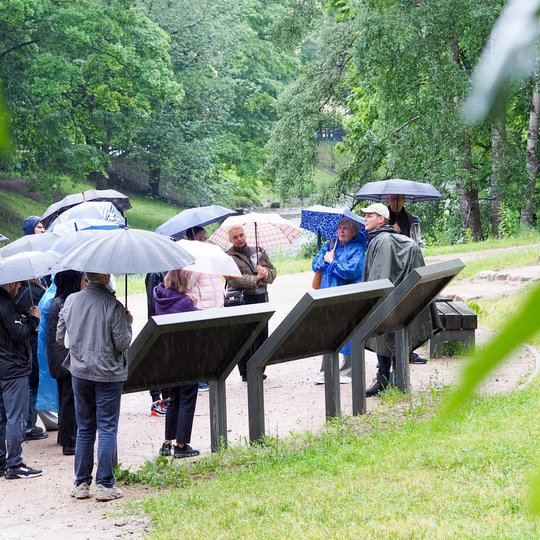 Nuotraukoje gidas veda ekskursiją apie legendų reikšmę vakaro lankytojams. Visi su skėčiais.