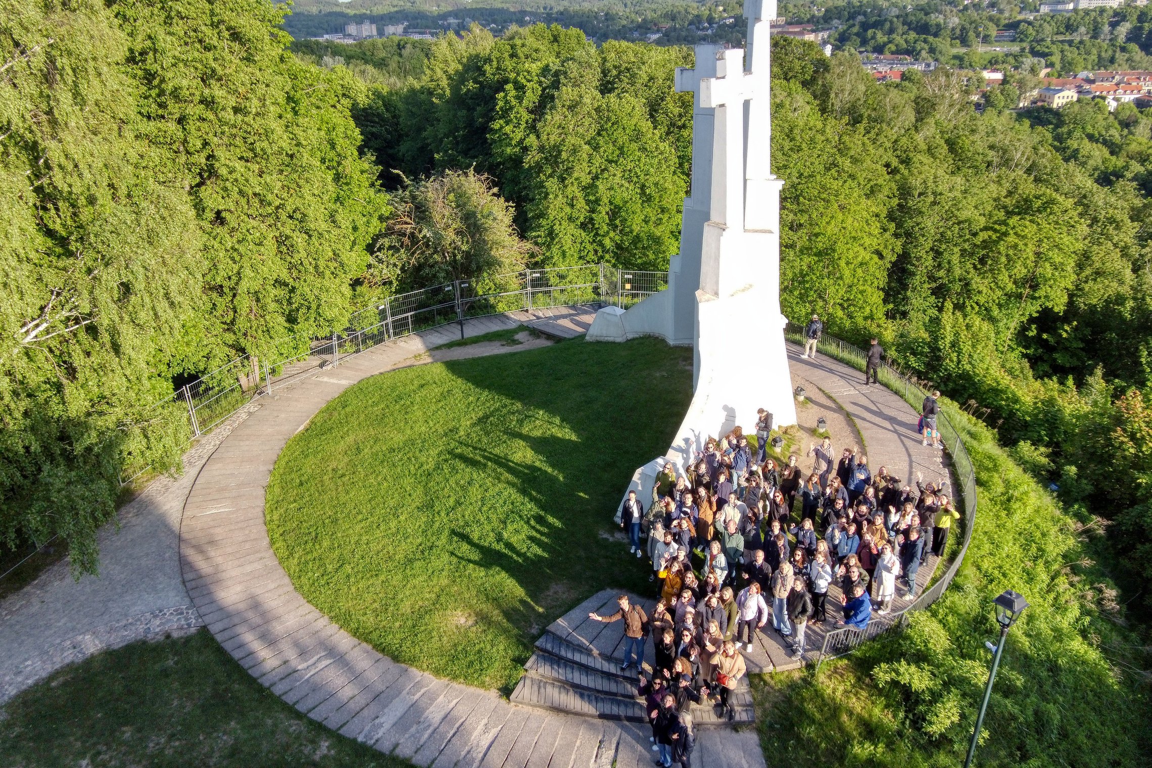 Grupinė ekskursijos nuotrauka Vilniaus pilių teritorijoje, prie Trijų Kryžių paminklo, žalios vasaros gamtos apsuptyje.