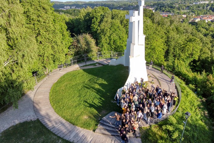 Grupinė ekskursijos nuotrauka Vilniaus pilių teritorijoje, prie Trijų Kryžių paminklo, žalios vasaros gamtos apsuptyje.