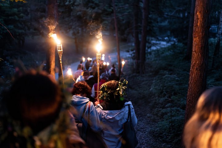 Žmonės su deglais vakare leidžiasi miško taku Vilniaus pilių teritorijos kalvomis.