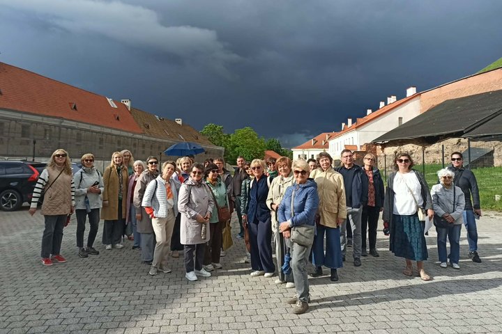 Ekskursijos dalyviai stovi Vilniaus pilių teritorijos kieme po dramatiškai tamsėjančiu dangumi.
