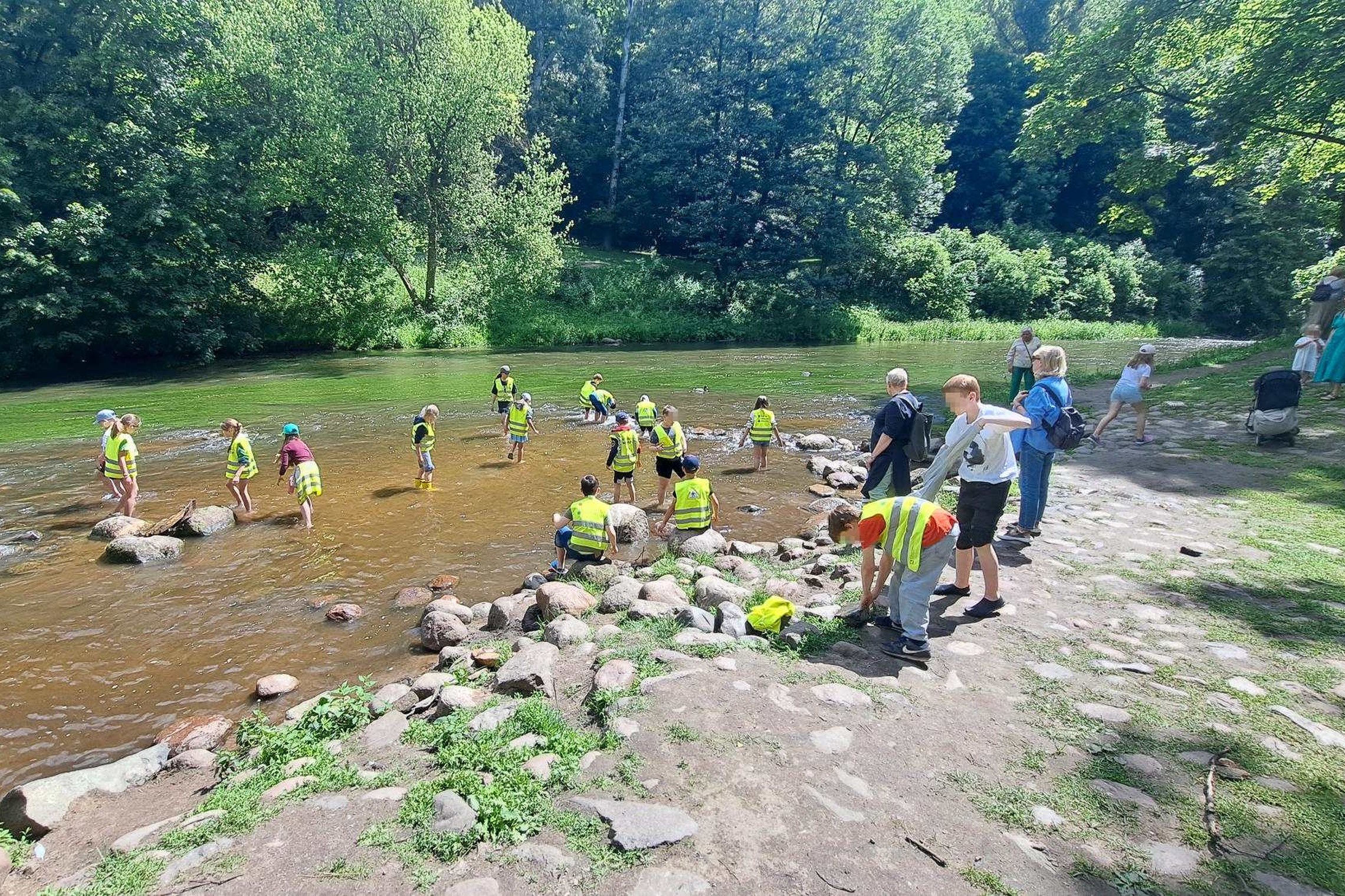 Vaikai su ryškiomis saugos liemenėmis dalyvauja Vilniaus pilių direkcijos povandeninės archeologijos edukacijoje sekliame upės ruože, ieško radinių tarp akmenų ir susipažįsta su archeologinių tyrimų principais gamtos apsuptyje.