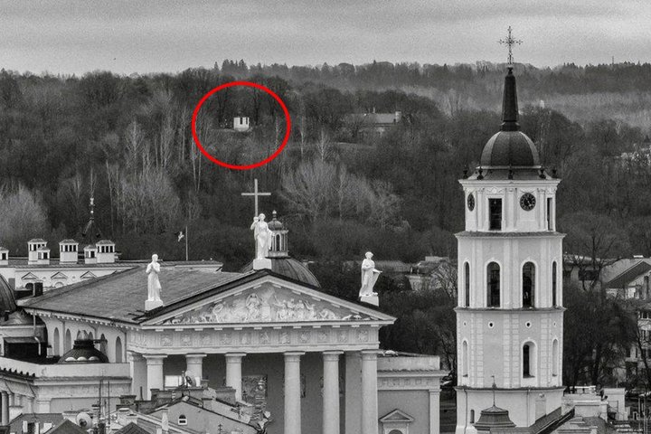 Juodai balta Vilniaus katedros ir varpinės nuotrauka su Vilniaus pilių kalvų fonu, raudonu apskritimu pažymėtas nedidelis šviesus bokštelis tarp medžių.