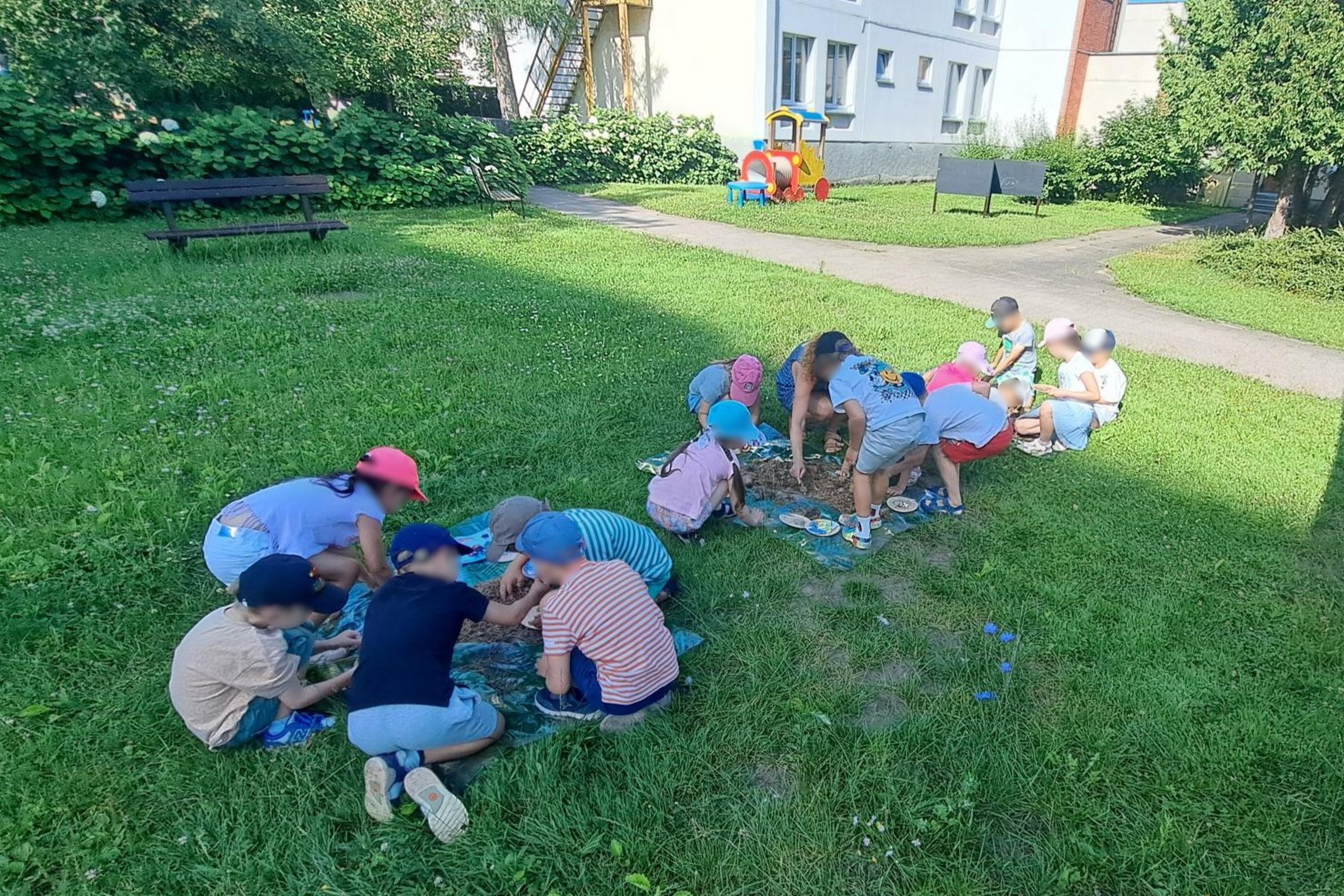 Nuotraukoje vaikai dalyvauja edukacijoje „Kasinėjant istoriją – skaitant žemės knygas“. Darželio kieme įrengtose tyrimų vietose jie ieško radinių.
