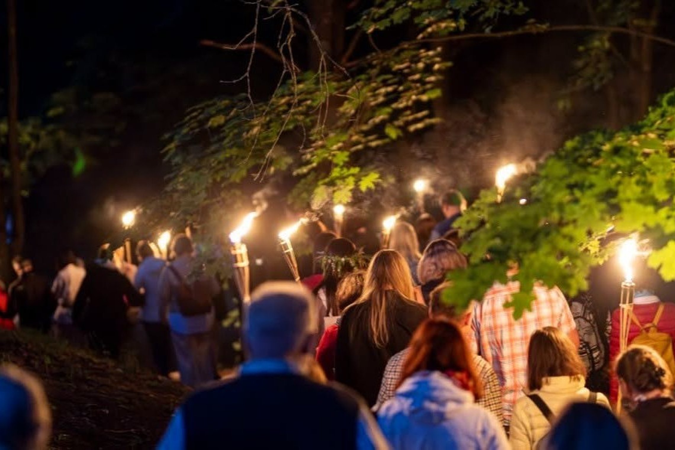 Žmonių grupė naktį eina per Vilniaus pilių teritoriją, rankose laikydama degančius fakelus.
