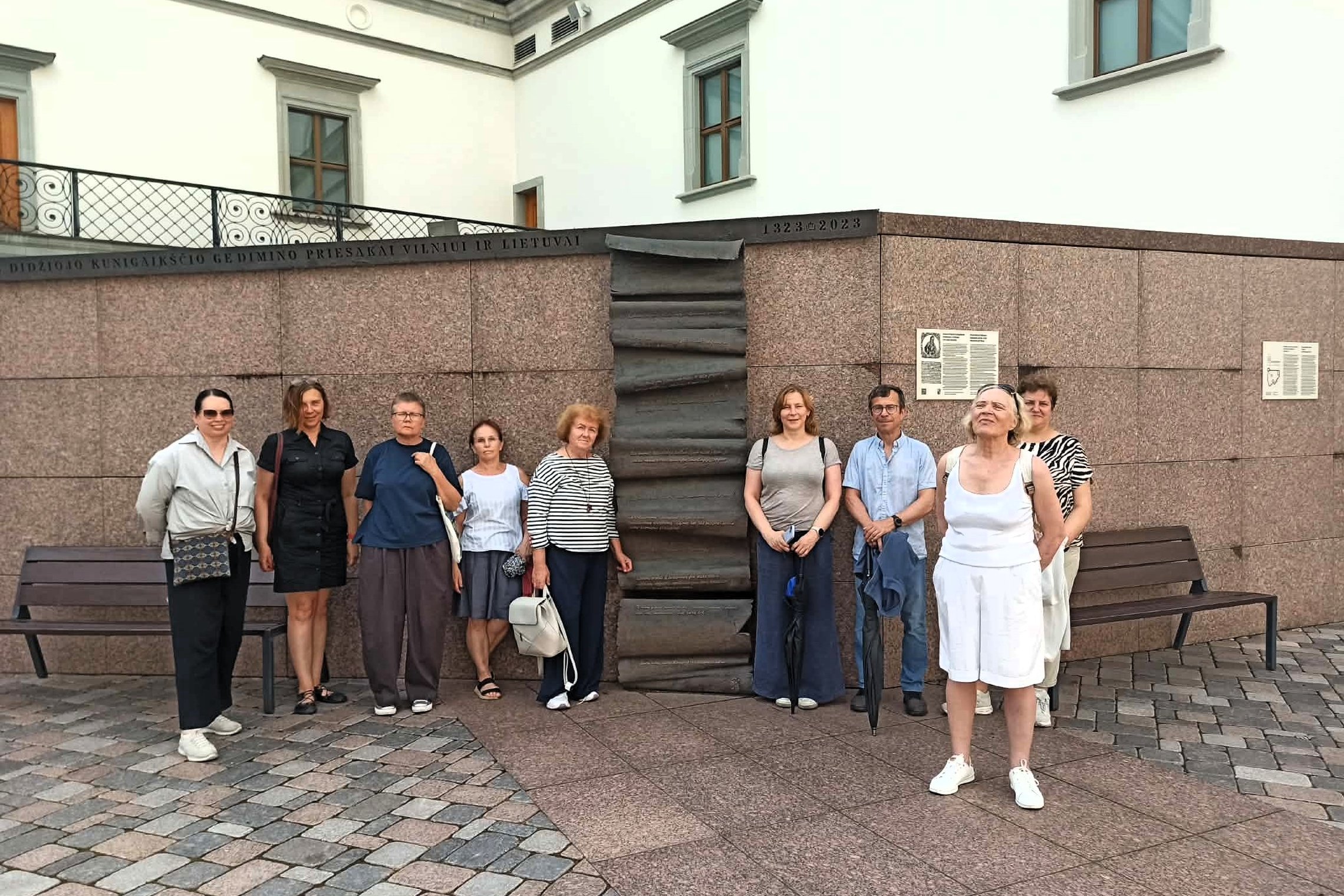 Ekskursijos „Menas atminčiai: Vilniaus pilių monumentai“ dalyviai pozuoja prie tikrosios Gedimino bokšto vietos ir Gedimino priesaikos Vilniui bei Lietuvai bareljefo.
